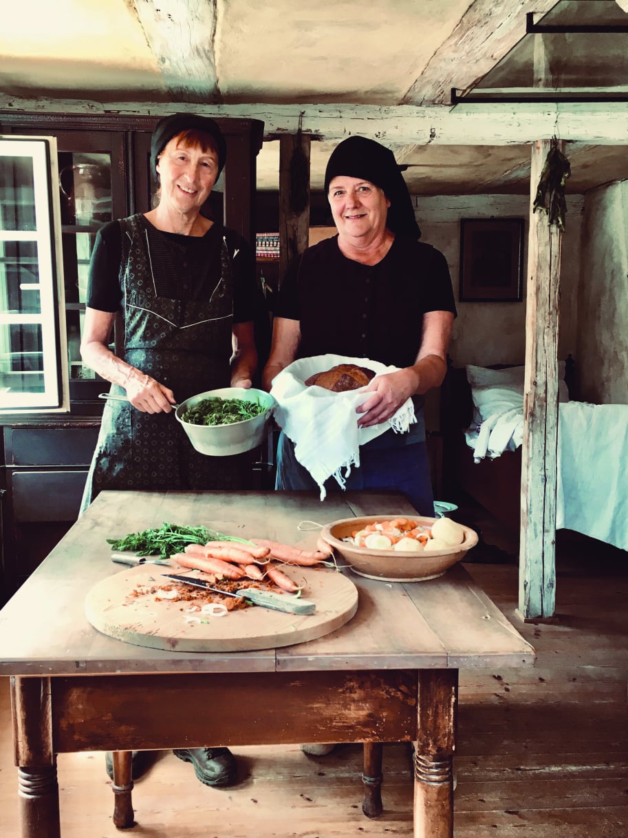 Zwei Frauen mit Kochutensilien und Gemüse am Museumstisch.